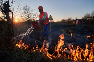 Fireman ecologist fighting wildfire in field with evening sky on background. Male environmentalist...