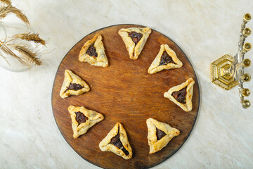 Gomentashi cookies traditional for the Jewish holiday of Purim on a wooden board next to the menorah and wheat ears.
