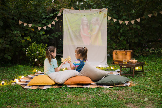 Outdoor Cinema Theater Backyard Family Outdoor Movie Night With Kids. Sisters Spending Time Together, Watching Cimema At Backyard DIY Screen With Film. Summer Outdoor Weekend Activities With Children