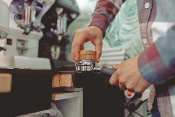 Close up of barista tamping ground coffee for making espresso