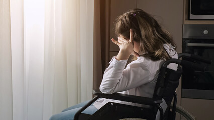 Pensive disabled woman with infantile cerebral paralysis sits in wheelchair near window behind curtain at home experiencing ableism, sunlight. - obrazy, fototapety, plakaty