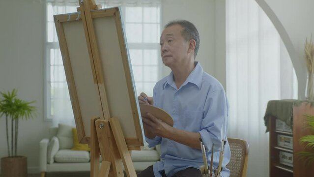 Older Asian men are happy together painting with watercolors on vacation at home, happy and laughing. Concentrate on drawing and appreciating your own work, the concept of creating art.