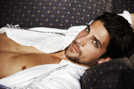 Radiating masculine confidence. Young attractive male, lying on a sofa looking at you with intensity.