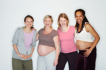 Pregnancy is a joy for them. Pregnant friends standing together while isolated on white.