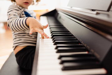 Pretty 3-year-old girl plays the keys of a piano and reads the sheet music with difficulty.