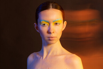 A woman's face in the blue and yellow national colors of Ukraine looks at the camera isolated on a dark background. Flag of UA, no war.