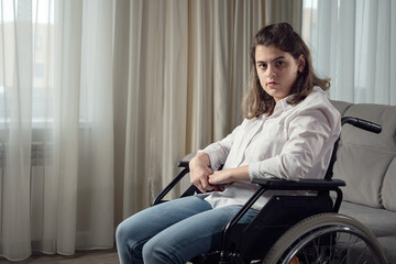 Sad disabled woman with organic damage of central nervous system sits in wheelchair looking at...