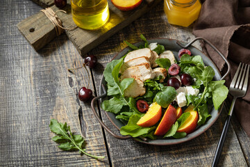 Healthy diet salad with grilled turkey, arugula, peach, cherry, feta and vinaigrette dressing on a rustic table. Keto diet lunch menu.  Copy space.