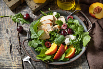 Healthy diet salad with grilled turkey, arugula, peach, cherry, feta and vinaigrette dressing on a rustic table. Keto diet lunch menu.