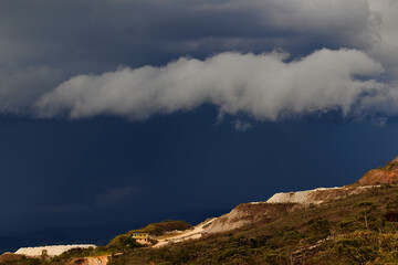 mountain with open pit mining sites under a stormy sky.