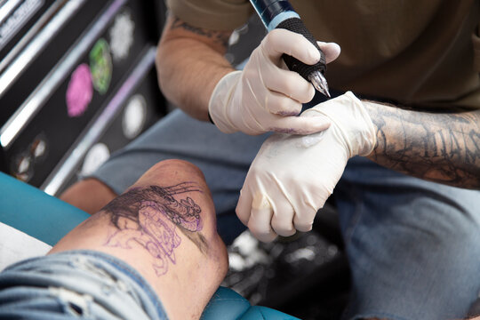 Anonymous tattooist making tattoo on leg of person