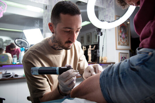 Tattooist making tattoo on leg of person