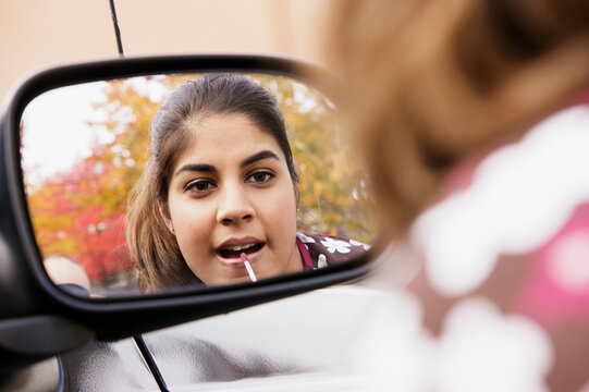 Young woman applying lip-gloss in rearview mirror