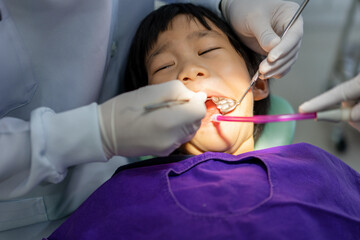 Fototapeta premium Hand of Doctor dentist is working on the teeth of asian little kid 6 year old patient in dental clinic