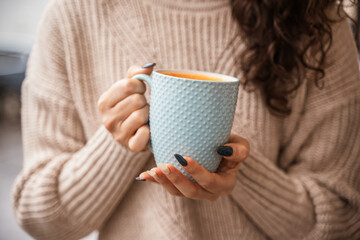 A girl in a beige sweater with a blue mug in her hands. Blue porcelain mug mockup for your design