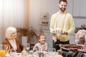 happy man with easter cake and painted eggs during easter dinner with family.