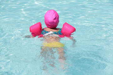 Criança na piscina a nadar com flutuador rosa com água azul.
