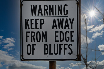 Warning Sign for Bluffs against a cloudy sky with a starburst