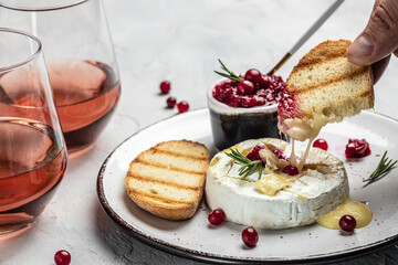 Baked camembert cheese with cranberries, basil leaves and rosemary on light table. French cuisine. Food recipe background. Close up