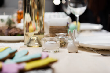 selective focus of decorative rabbit and candle near blurred cookies and bottle of wine.