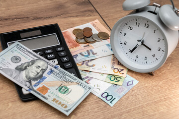 Banknotes and coins of the Republic of Belarus, one hundred US dollars, an alarm clock and a calculator on a wooden background. Belarusian monetary inflation. Time to change money.