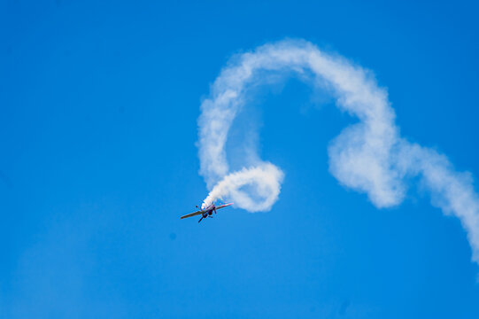Small single engine stunt plane trailing smoke filled loops across a deep blue sky.