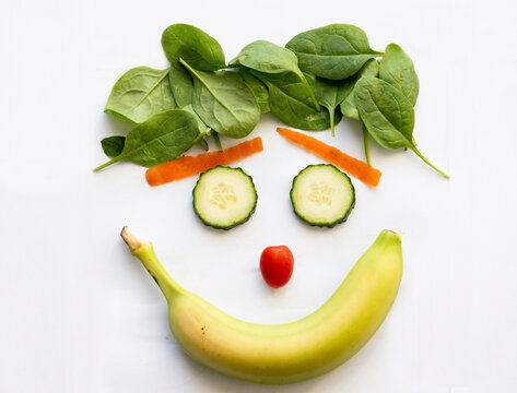 A smiley face made of a banana, cheery tomato, cucumber, carrot shavings and spinach on a white background. photo Graham Hughes