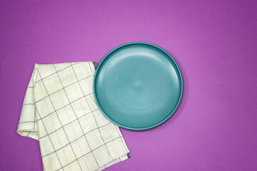 empty ceramic blue plate on purple background with plaid napkin