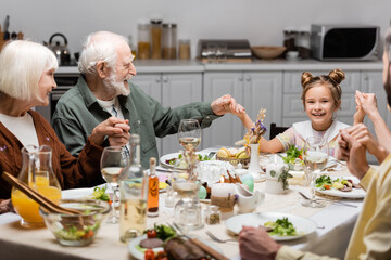 cheerful family holding hands while sitting at table with easter dinner.