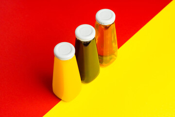 Bottles with yellow and red liquid halthy beverage on yellow and red background. Orange apple cherry