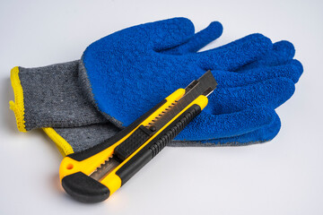 blue rubberized work gloves and a stationery knife lie on a white background