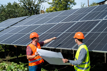 near the new solar panels, two young workers in uniform stand with a plan of work performed