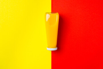 Bottle with yellow liquid halthy beverage on yellow and red background. Orange fresh drink
