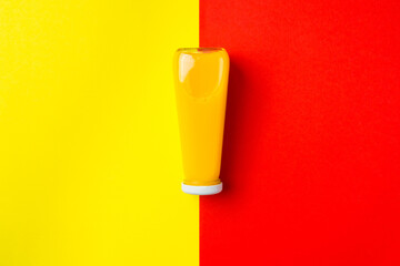 Bottle with yellow liquid halthy beverage on yellow and red background. Orange fresh drink