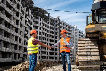 two good workers in uniform shake hands near the grader and the new building