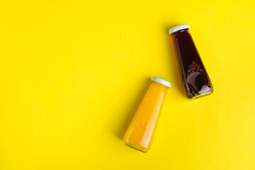 Bottles with yellow and red liquid halthy beverage on yellow background. Orange and cherry juice