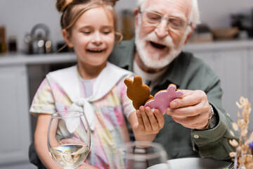 amazed girl with grandpa holding easter cookies during celebration at home, blurred background.
