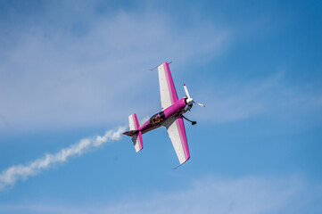 Single engine stunt plabe flying and creating smoke patterns in the blue sky.