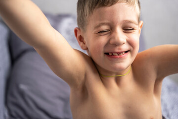 Portrait of a cute 5-year-old Caucasian boy who has just woken up and is stretching on the bed.