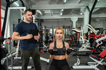  young trainer with inflated biceps trains a young cute brunette client for body health.