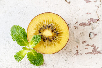 Ripe raw kiwi gold slice with mint leaves  closeup on grunge white stone table.
