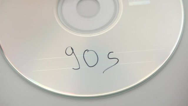 female hand writing 90s on compact disc with black pen, closeup static shot
