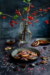 Beautiful spring composition. Homemade cookies with colorful sprinkles and viburnum branches with berries in a vase on a dark background. Vertical