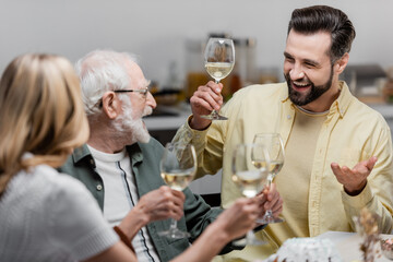 senior man holding glass of wine while celebrating easter with adult son and daughter.