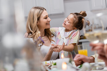 cheerful mother and daughter holding hands and looking at each other during easter celebration.