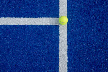 Close-up of a tennis ball on the white line of a paddle tennis court