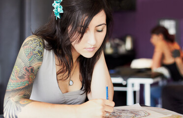 Coming up with some great designs. A female tattoo artist drawing a new design while in her tattoo...