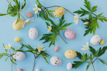 Colorful Easter chocolate eggs and spring flowers flat lay on blue background. Stylish easter background and greeting card. Happy Easter! © sonyachny