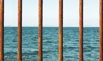 Rusty iron railing of a prison with beautiful sea and white sky background. End of the road, no more way concept. Metaphoric or analogical expression of the opposition between freedom and captivity.