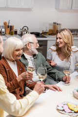 happy woman talking to senior parents holding glasses with wine during easter dinner.